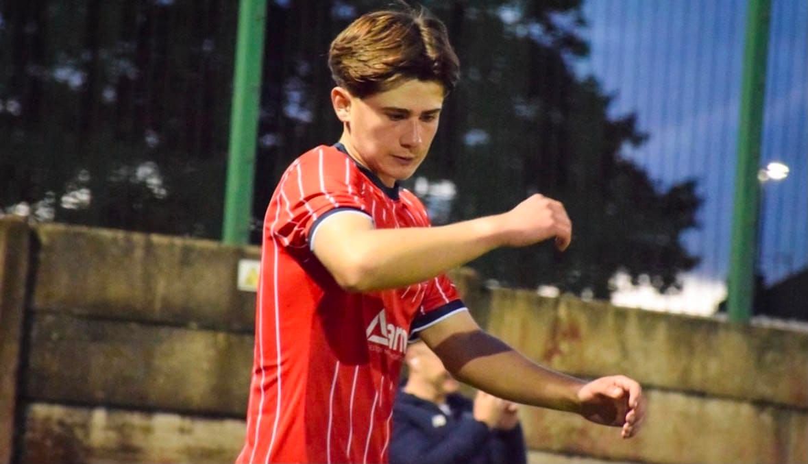 A player in a red and white striped kit concentrates during a match under floodlights