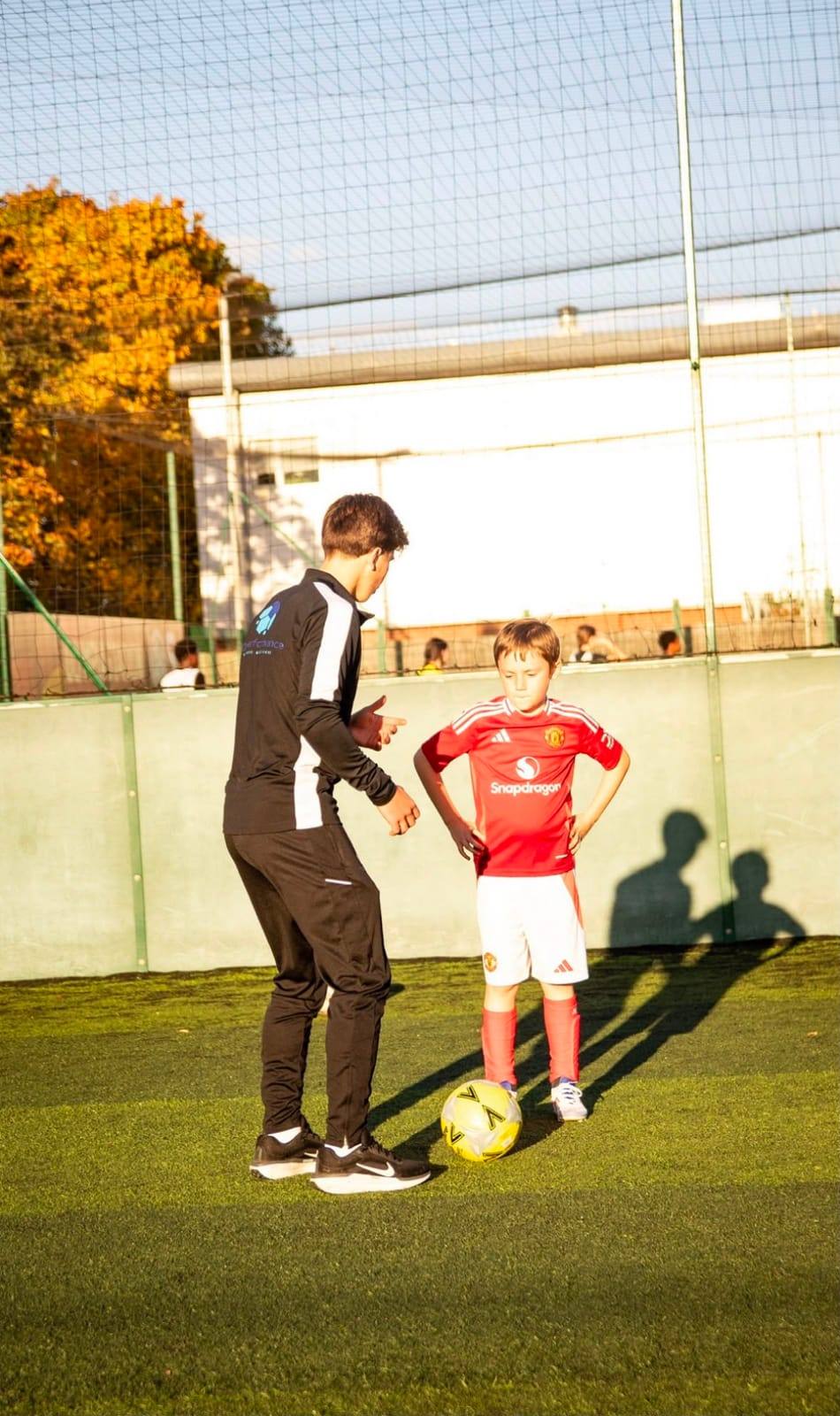 A coach in HDperformance kit talks a young player through a drill on a sunny 4G pitch